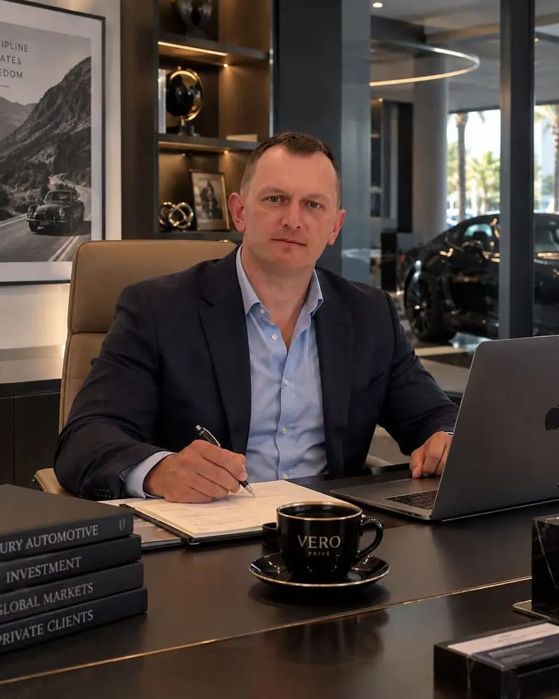 Michael at his desk, a Porsche in the showroom behind him